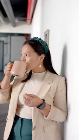 vertical video: drinking coffee, woman in office attire taking break against wall
