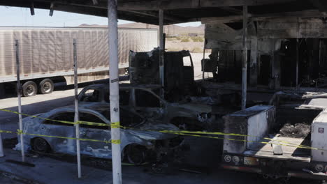 burnt out cars and trucks behind police tape at scene of gas station fire