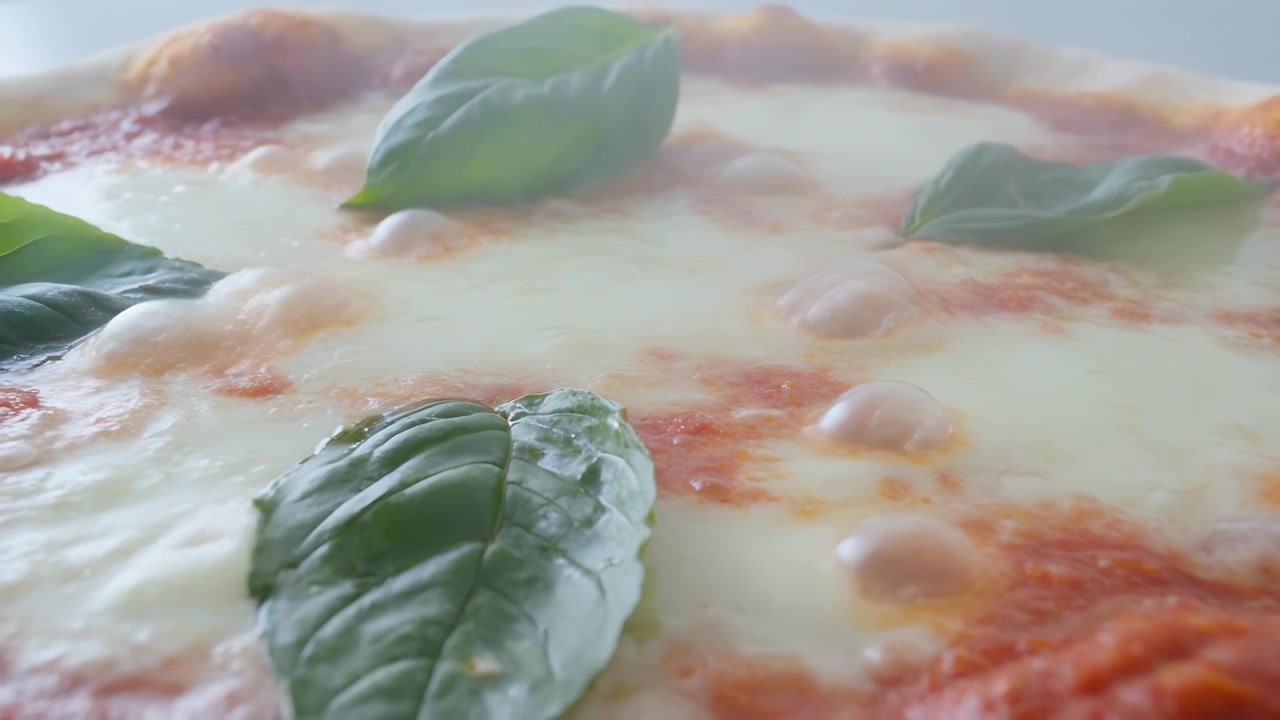 Telecamera che si allontana rivelando una pizza su un piatto chiaro per mostrare crosta, mozzarella, pomodoro, basilico, vapore