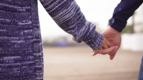 Vista-De-Cerca-De-Una-Pareja-Joven-En-La-Playa-Tomados-De-La-Mano-Y-Caminando-Juntos.-Tiro-En-Cámara-Lenta