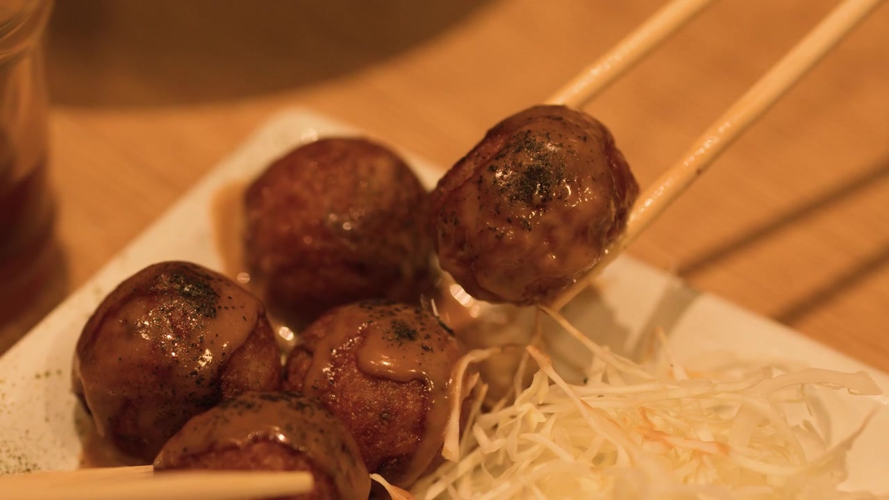 タイのバンコクで、白い皿からたこ焼きを木製の箸で持ち上げるクローズアップ