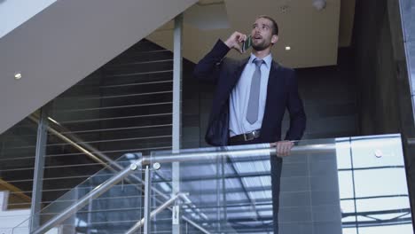 hombre de negocios hablando por teléfono móvil cerca de la escalera en la oficina 4k