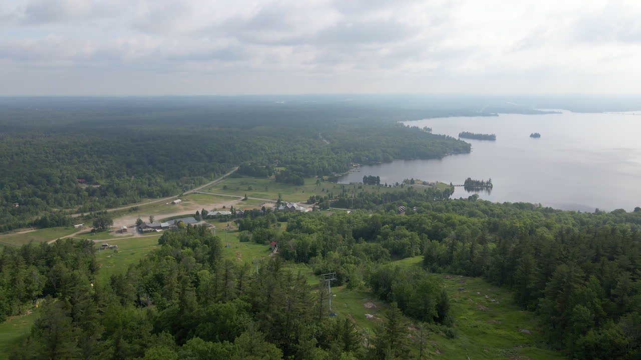 Aerial shot over campsites on side of tree covered mountain at edge of lake. Calabogie ski hill. Ontario Canada