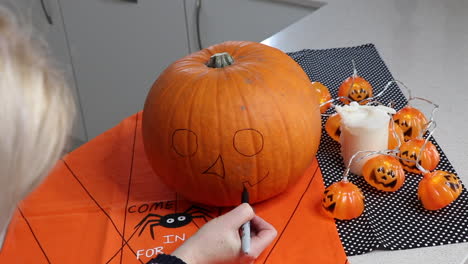 mujer dibujando cara espeluznante en una calabaza naranja en casa en la cocina