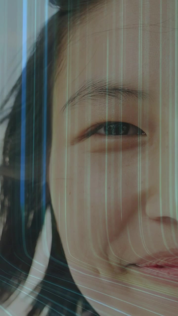 Vertical video: Adult woman smiling while earbud triggers light streaks moving across face in tech