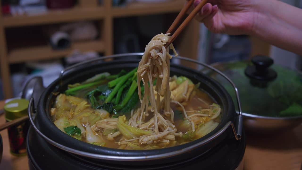 Bacchette che prelevano funghi Enoki da un hot pot giapponese