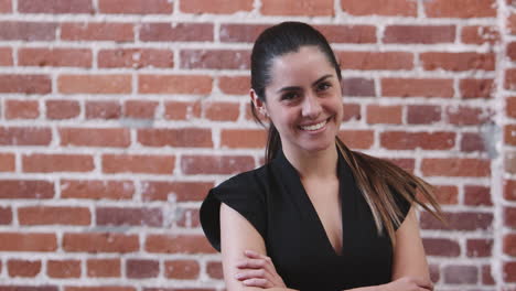 portrait of smiling businesswoman standing against brick wall in modern office