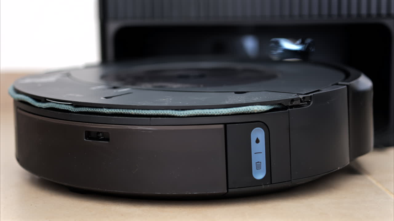Close up of a black robot vacuum cleaner moving and rotating on the floor tiles
