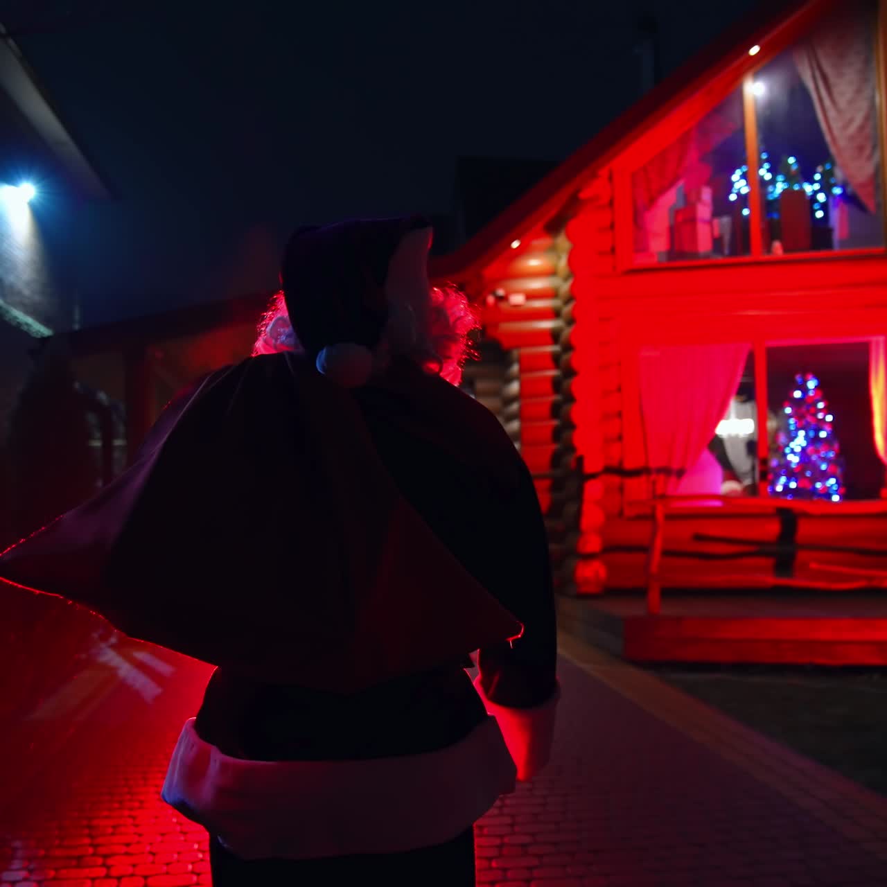 Santa Claus walking on pavement. Father Frost at Christmas outdoors. Santa walking on a pavement at dark. Red lighting. Back view