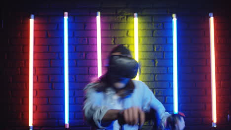 close up view of young man in vr glasses and playing a virtual game in a room with colorful neon lamps on the wall