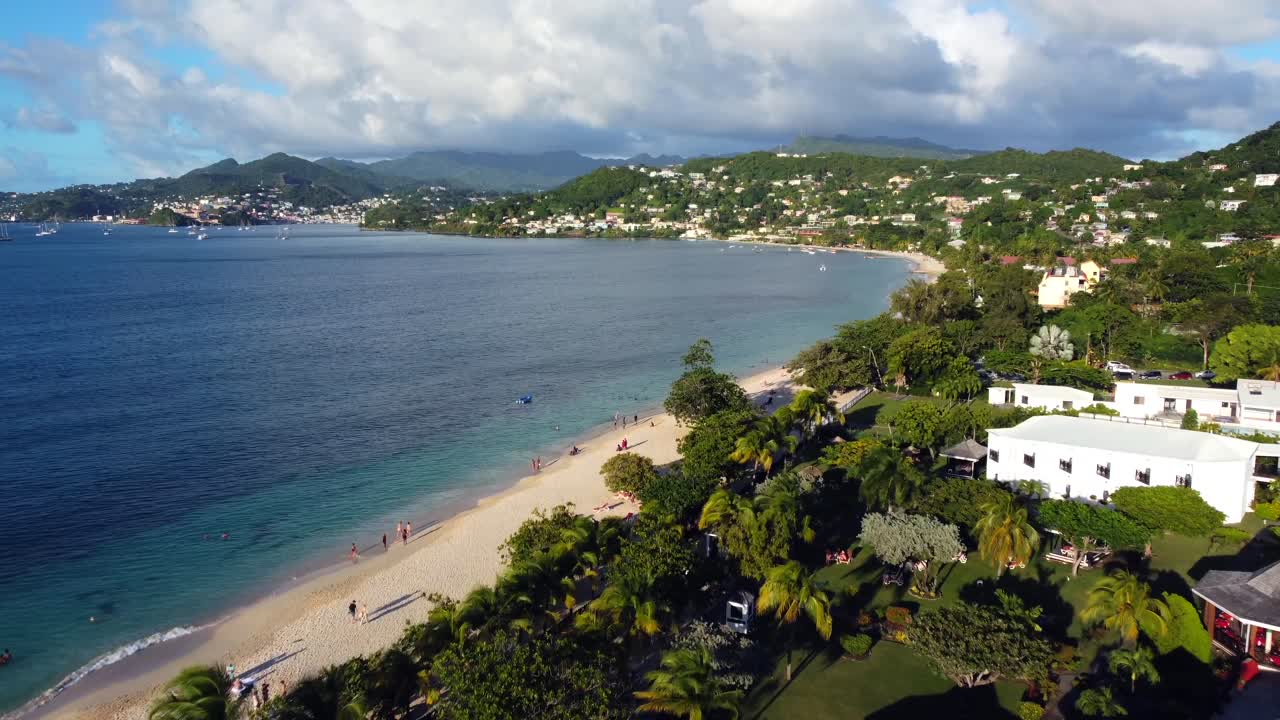Aerial shot overlooking little town with green hill properties and curved Grand Anse Beach