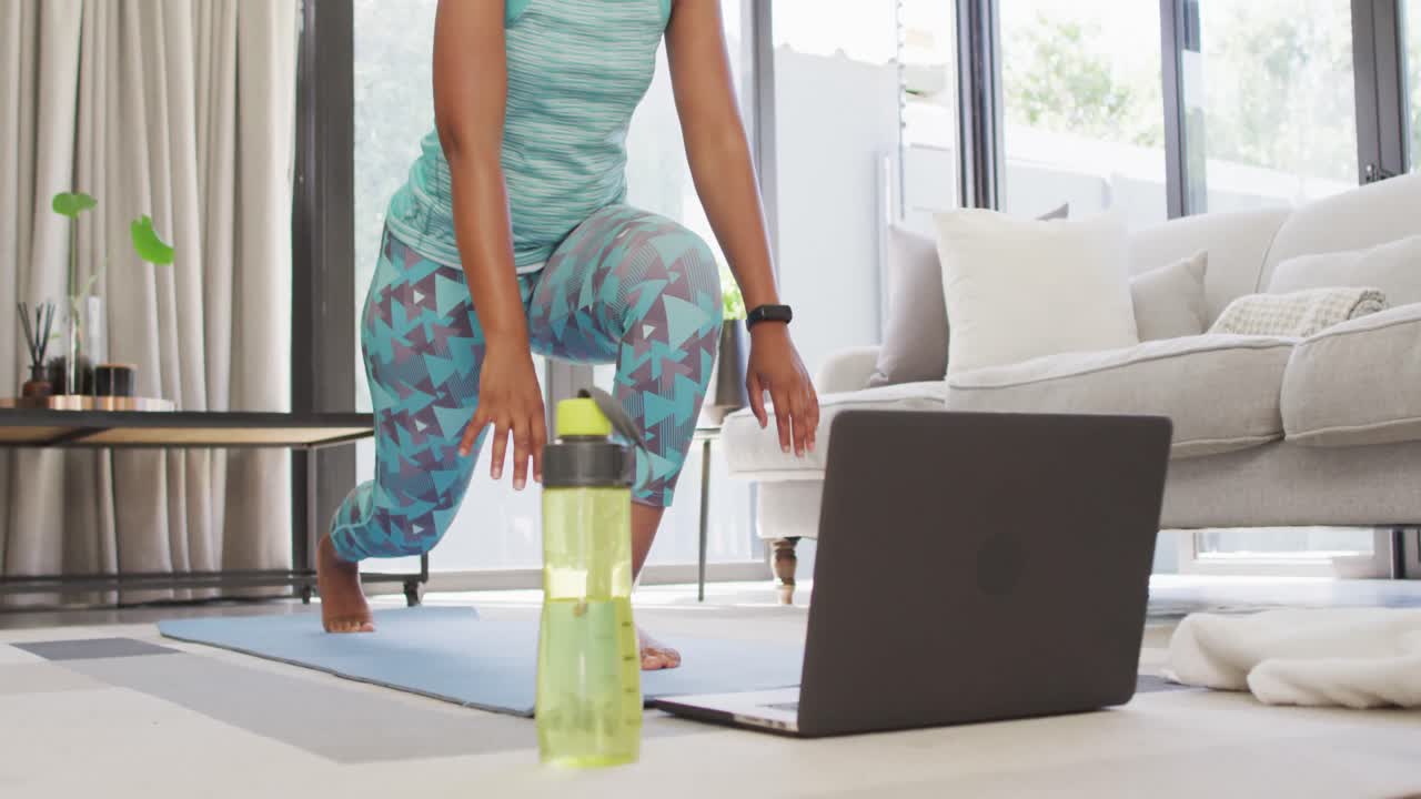 feliz afroamericano usando ropa deportiva, haciendo ejercicio, usando una computadora portátil