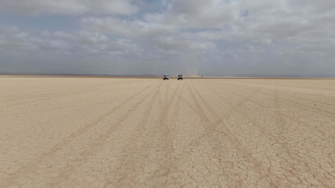 Vista drone di guida fuoristrada attraverso un paesaggio desertico isolato con ampi spazi aperti, ripresa aerea bassa che si avvicina ai veicoli. Gibuti, Africa