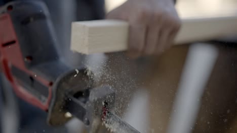 Close up slow motion shot, cordless reciprocating saw cuts through plank or batten