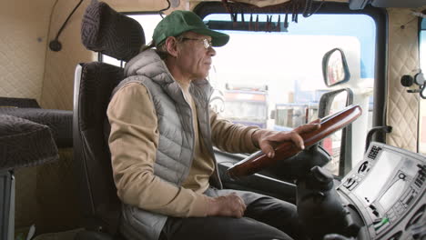 side view of older worker wearing cap and vest driving a truck in a logistics park