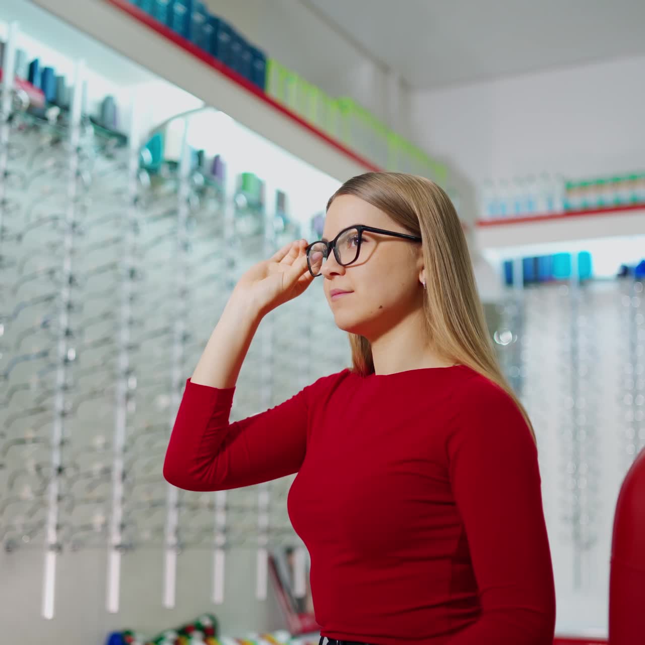 Beautiful female choosing glasses in the optical store. Young woman buyer trying on new eyeglasses. Eyesight concept.