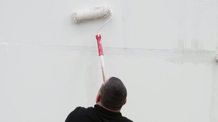 Paint roller applying white paint on a wall