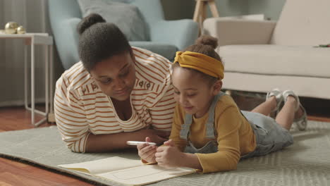 african woman watching her little daughter drawing