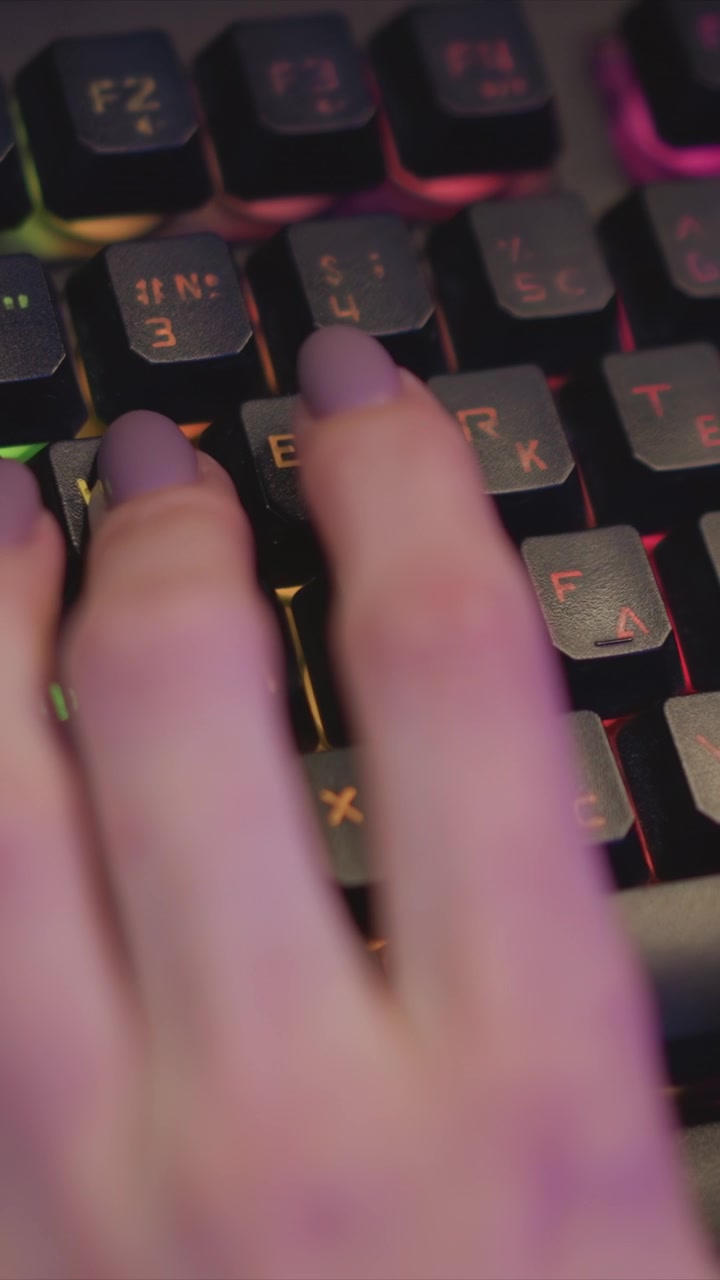 Close-up de mão com esmalte lilás digitando em teclado mecânico iluminado. Os dedos pressionam várias teclas, incluindo E, Y e F4, contra um fundo com iluminação suave e brilhante