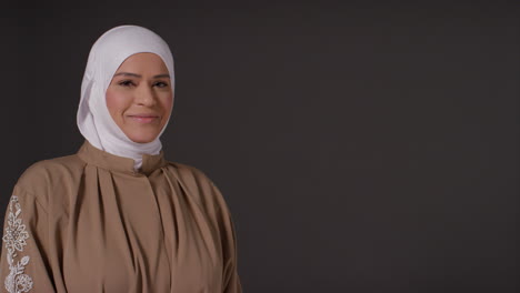 studio portrait of smiling muslim woman wearing hijab against plain dark background 2