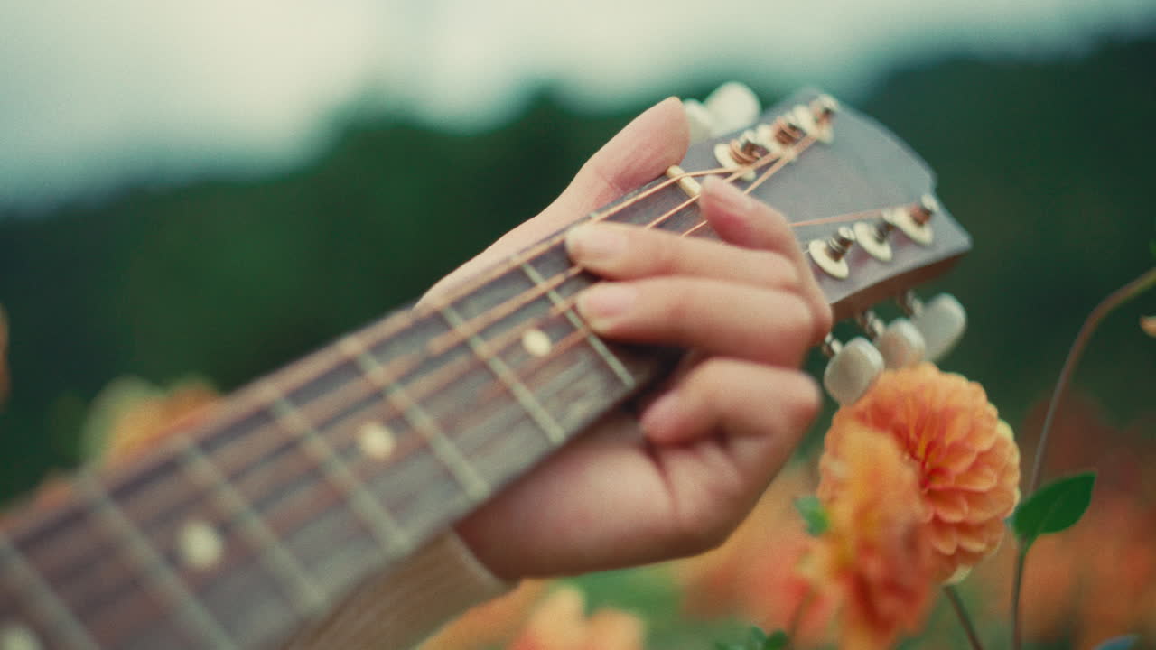 Primo piano di una chitarra acustica suonata all'aperto con fiori arancioni sullo sfondo, che unisce musica e natura in una scena rilassante