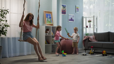 young mother rides swing while kids play with toy swords