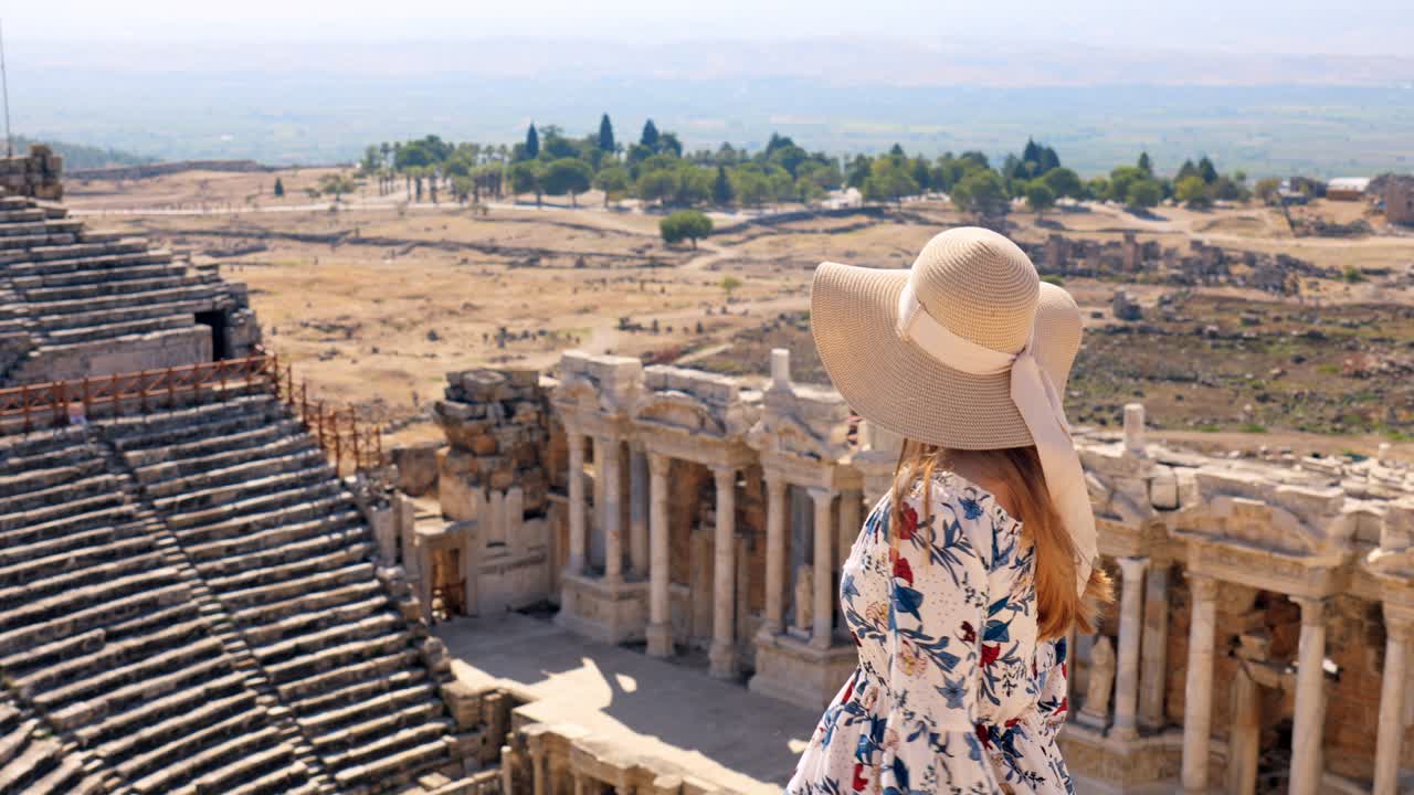 Stunning video of a young white caucasian ginger girl standing at the Roman amphitheater at the ruins of Hierapolis, in Pamukkale, Türkiye. UNESCO world heritage. Video was made on sunny summer day.