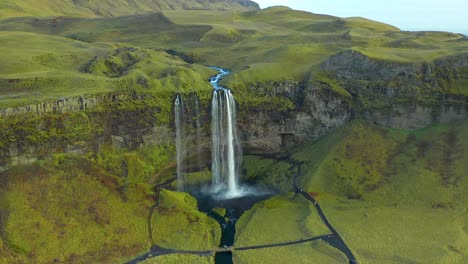 scenic view of waterfall cascade in green plateau landscape, aerial push in shot in seljalandsfoss iceland