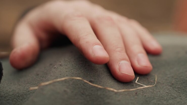 Intime Nahaufnahme einer Kinderhand, die mit der Fingerspitze eine helle Kreide- oder Staublinie auf einem gedämpften grünen, strukturierten Stoff entlangfährt, was sanftes Nachzeichnen, taktile Erkundung, weiches Licht und Stille zeigt.
