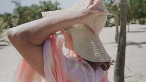 gelukkige oudere blanke vrouw zit in een ligstoel op een zonnig strand en draagt een zonnekap, in slow motion.