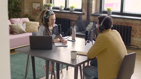 young man and woman sitting at a table with microphones and computer while recording a podcast