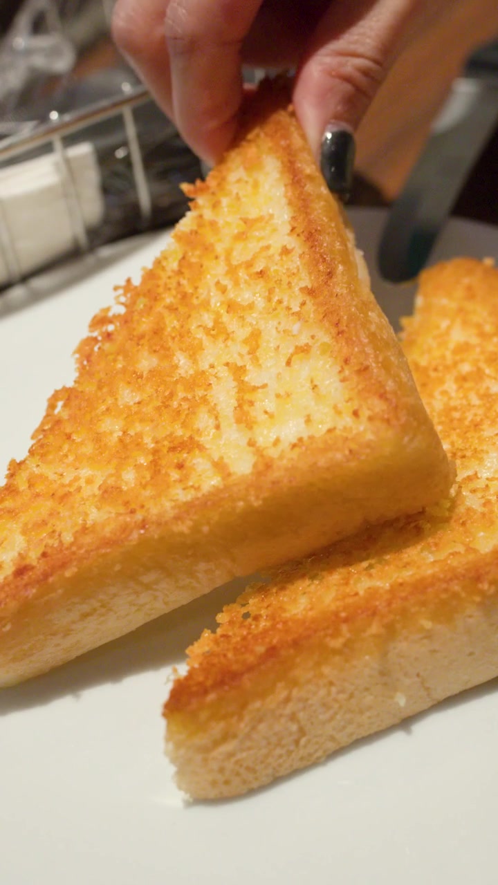 Close-up of hand grabbing golden garlic bread slices on white plate in warm restaurant lighting