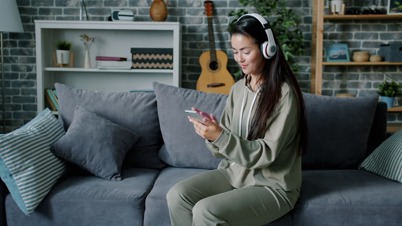 여성이 헤드폰과 전화로 소파에서 휴식을 취하고 있습니다.
