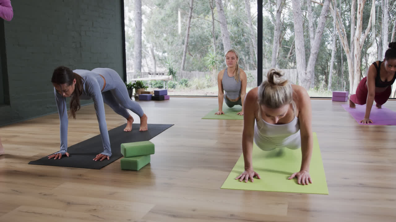 mujeres diversas en pose de cobra enfocadas juntas en esteras en clase de yoga con entrenadora femenina, cámara lenta