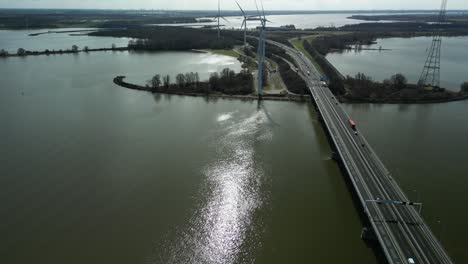 Drone-flies-backwards-above-a-river-next-to-a-bridge-with-a-national-road