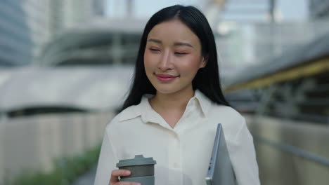 young asian businesswoman walking in city with coffee and laptop