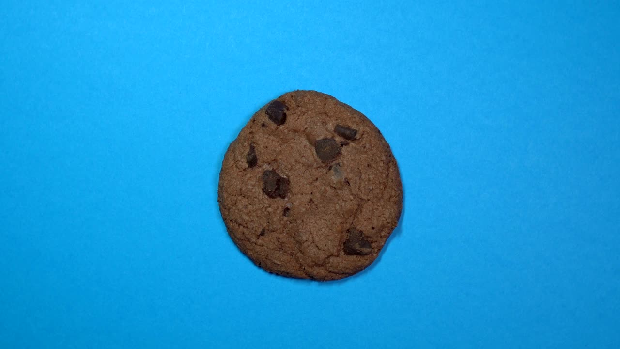 Chocolate chip cookie close-up, macro shot, slowly spinning on a rotating blue background.