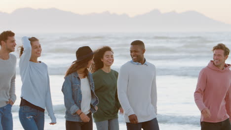 group of friends walking along winter beach together