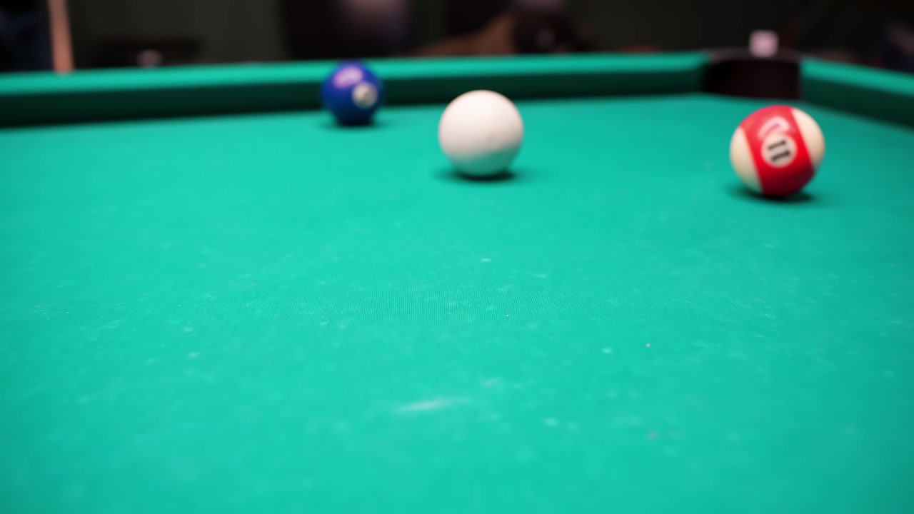 Shallow focus shot of yellow 1 and black 8 on green baize billiards table, cue ball nearby in a cozy game room with cinematic bokeh.