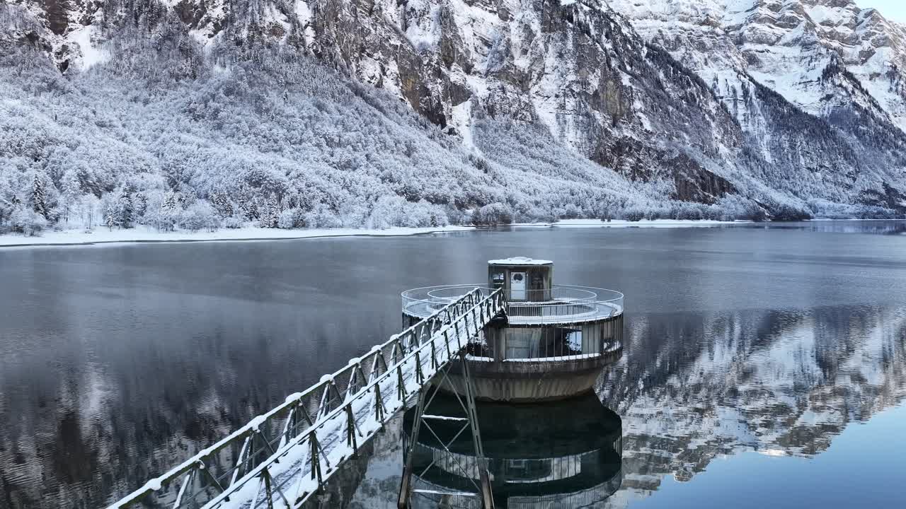 Snow covered water intake tower on Klöntalersee with winter alpine reflections