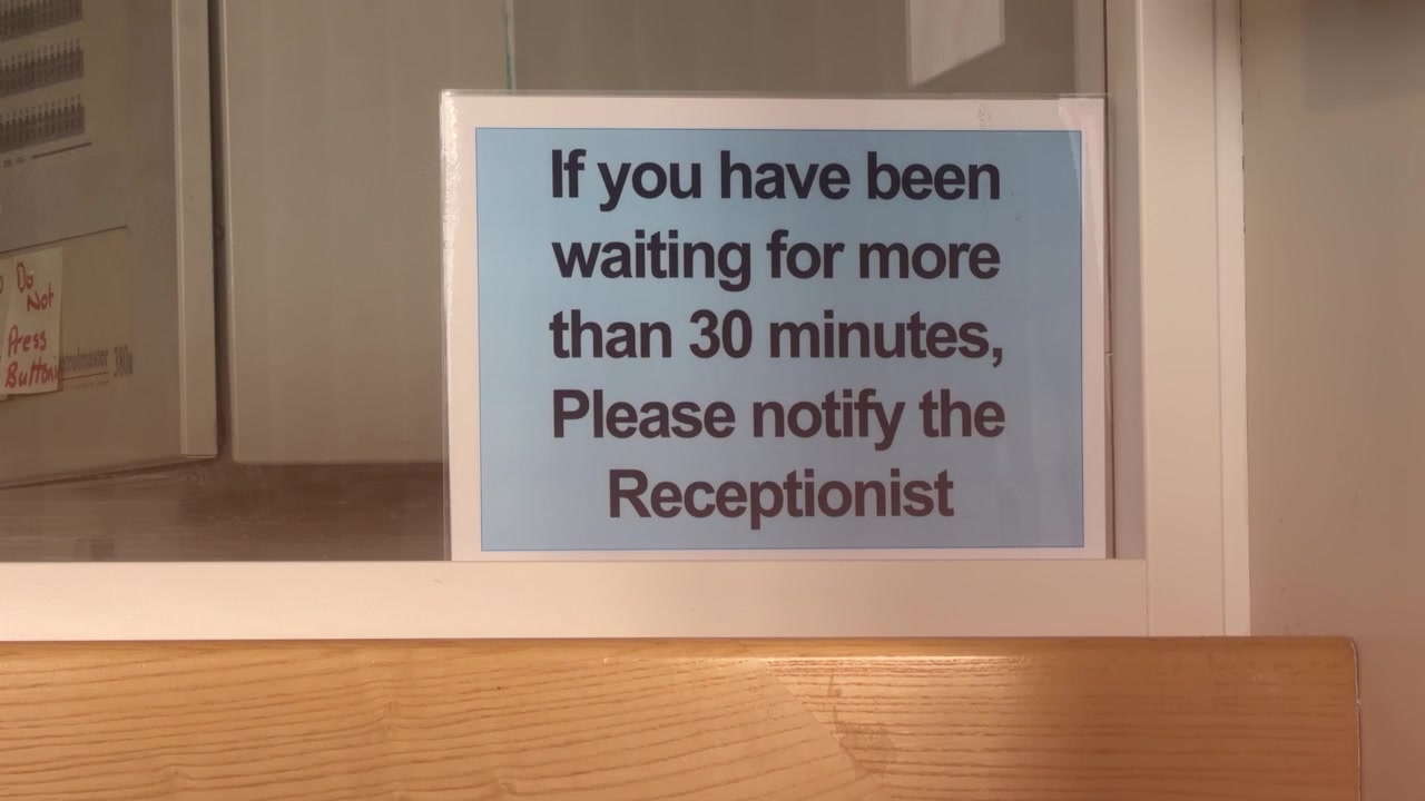 Vista ravvicinata, avviso alla reception a Kilmarnock, Scozia, che consiglia ai visitatori che hanno atteso più di 30 minuti di informare la receptionist