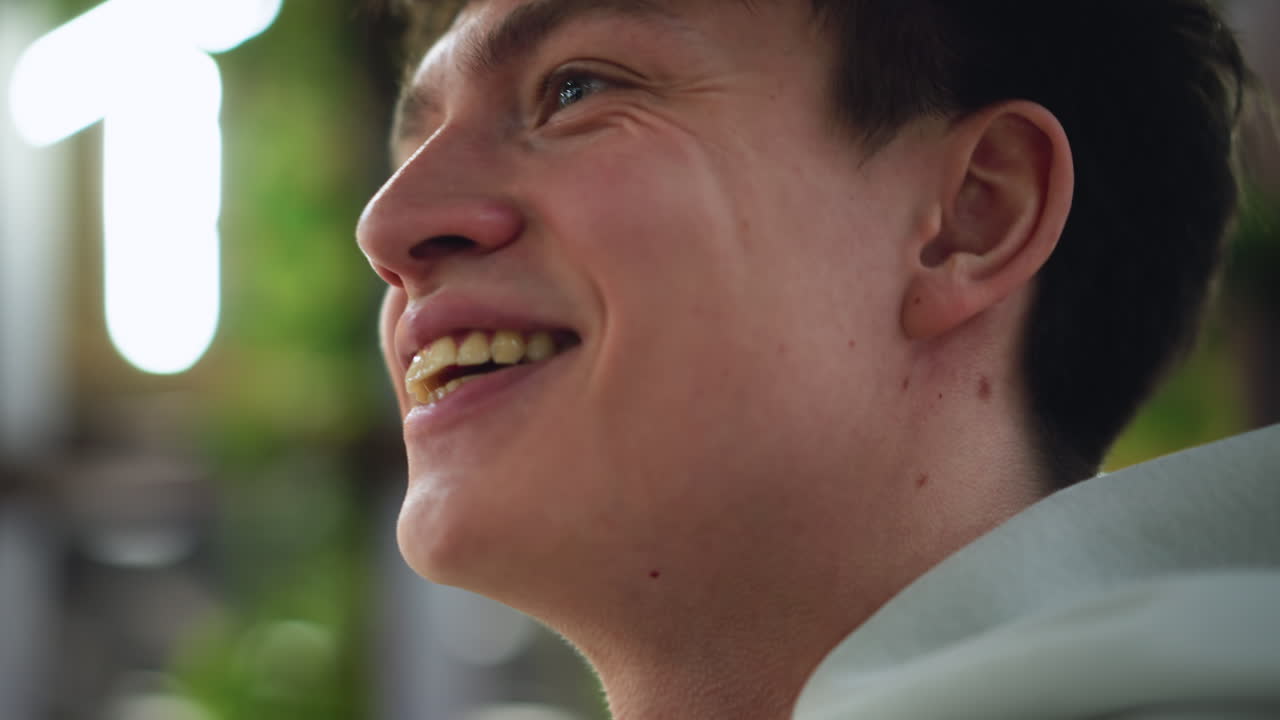 White young man smiling broadly showing teeth and long nose, camera capture of expressive face, warm light and soft background, joyful eye contact conveying genuine happiness and friendly connection