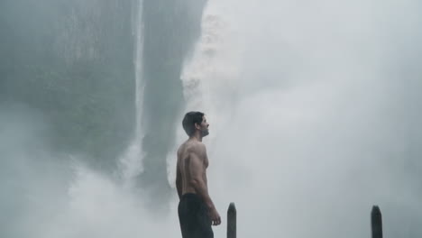 elated man celebrates in front of massive bajos del toro waterfall in monsoon rain