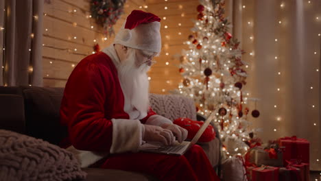 el verdadero papá noel se prepara para la navidad y hace un itinerario en su computadora portátil sentado en casa en la víspera de navidad. preparación para la entrega de regalos para navidad