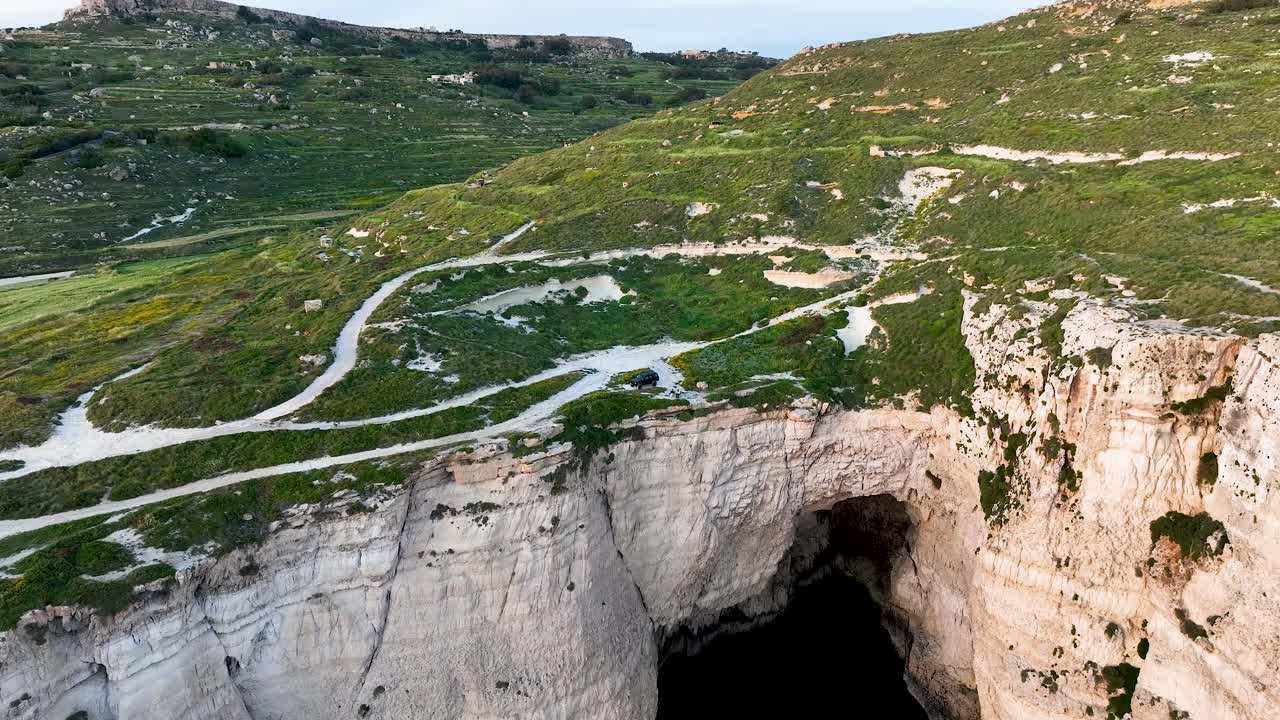Aerial shot reveals a large coastal cave set in Migra l-Ferha’s towering limestone cliffs, surrounded by lush countryside, showcasing Malta’s unique geology and wild scenery.