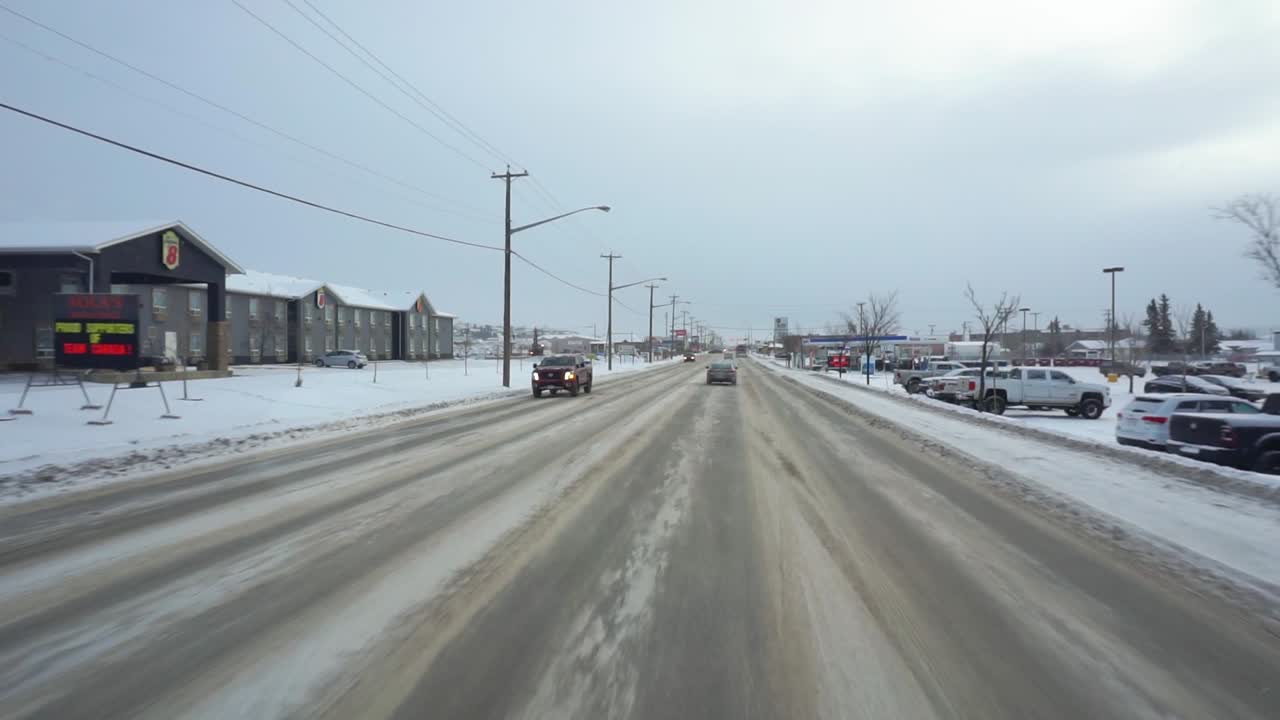 Pov shot driving in Dawson city, passing cars and snowy streets, winter day, in Yukon, Canada