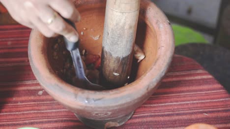 cooking som tam series: slo mo street food vendor's hand mixing som tam or thai spicy green papaya salad ingredients in mortar using pestle and ladle at street food shop