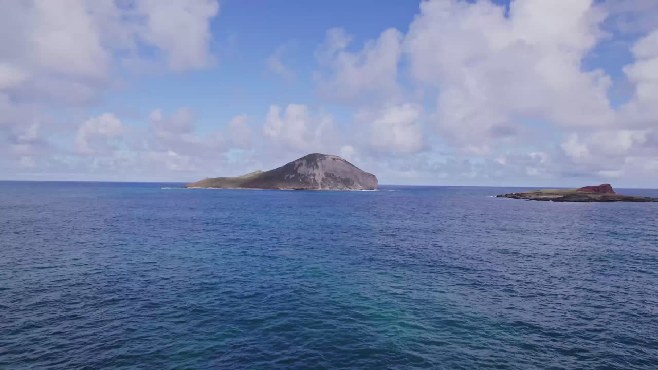 drone footage skimming the blue water pacific Ocean towards an island near Oahu Hawaii revealing craters in the volcanic formation
