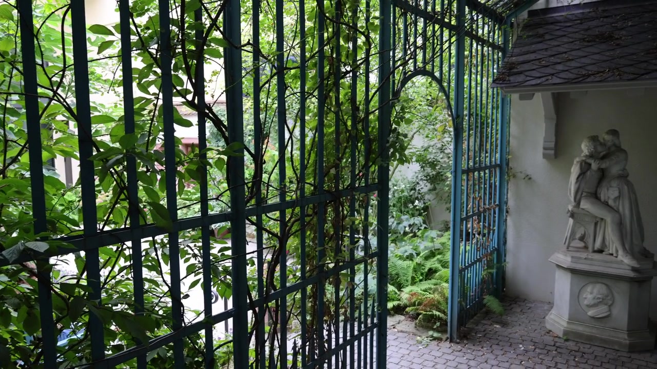 Almanya, Frankfurt'taki Goethe Evi'nin bahçe köşkündeki Werther heykeli. Kamera hareketi, figürü tarihi bahçe ortamında gösteriyor.