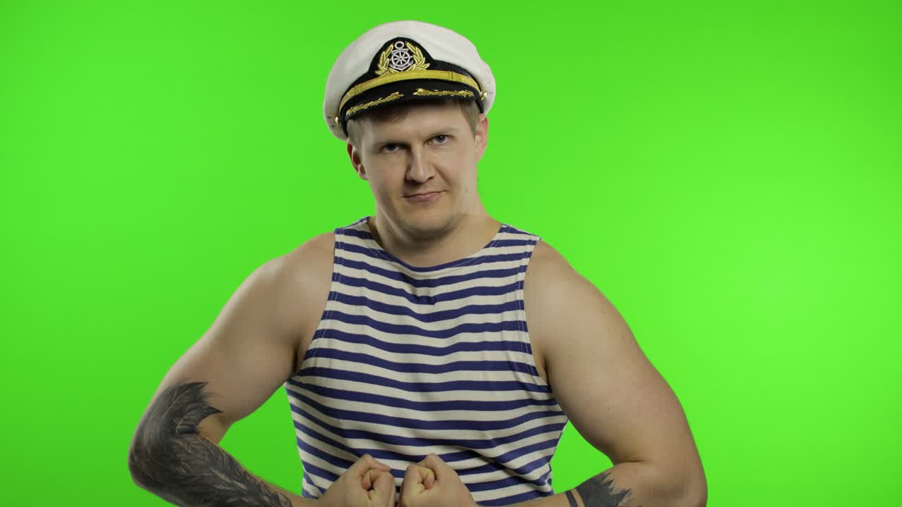 молодой моряк показывает мышцы, глядя в камеру. моряк в моряцком жилете